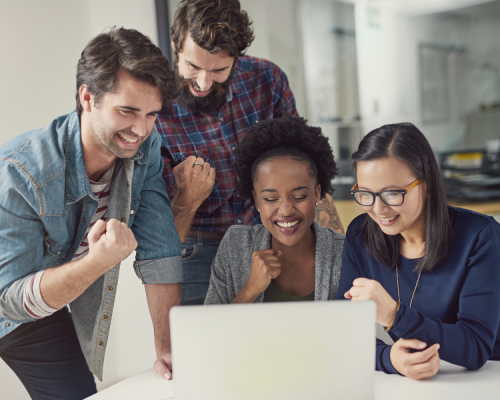4 junge Menschen, die gut gelaunt zusammen etwas auf einem Laptop anschauen